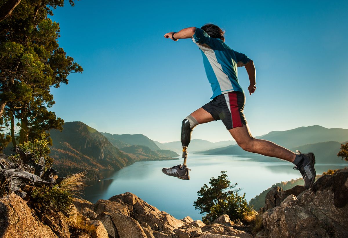 Ein Mann mit Beinprothese joggt über steiniges hügeliges Gelände an einem Gewässer.
